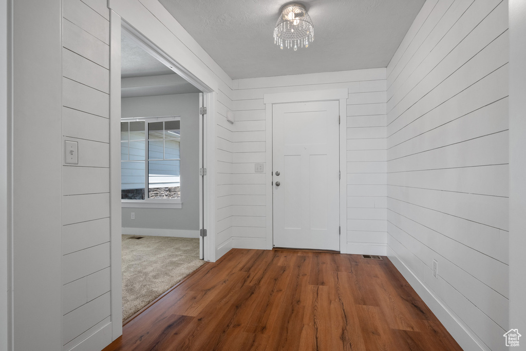 Foyer featuring a chandelier, wood walls, dark wood-style floors, and baseboards