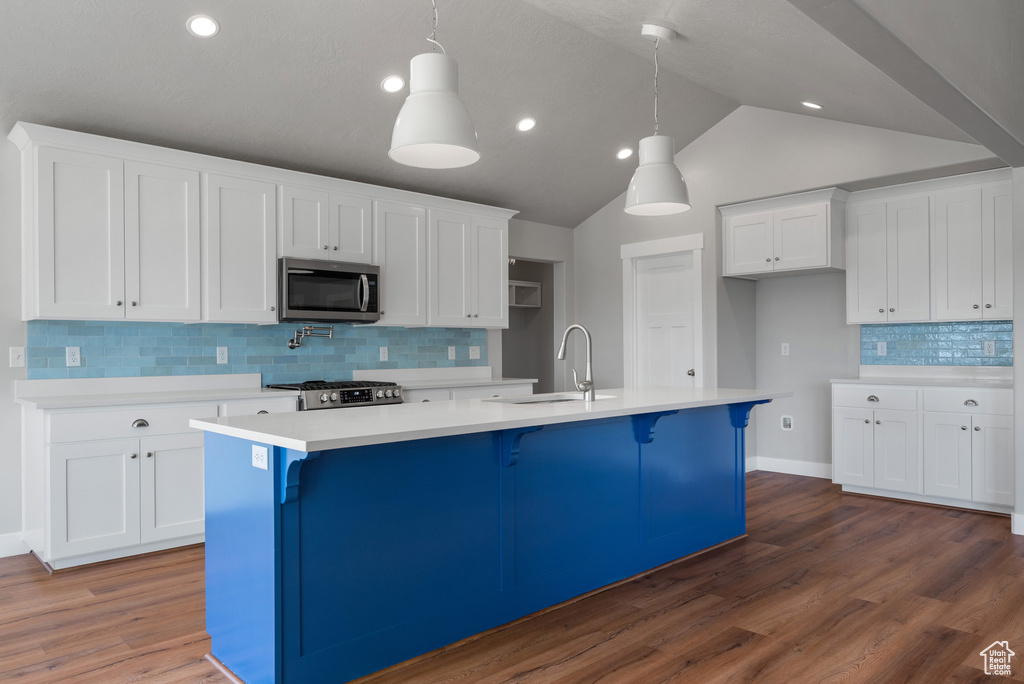 Kitchen with stainless steel microwave, a sink, stove, white cabinets, and vaulted ceiling