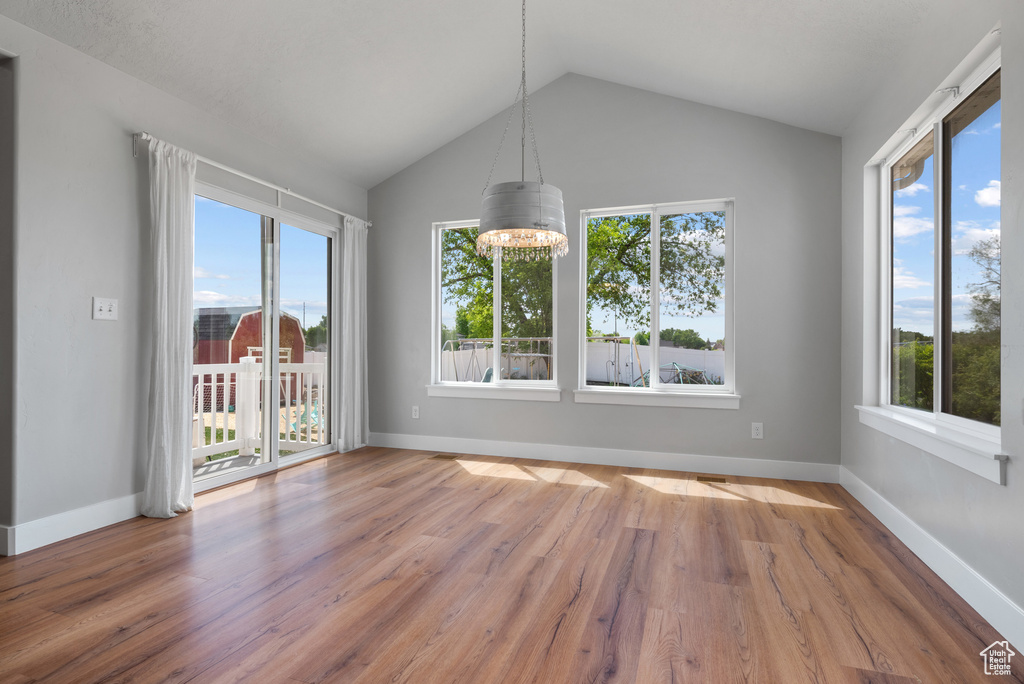 Unfurnished dining area with healthy amount of natural light, vaulted ceiling, wood finished floors, a chandelier, and baseboards