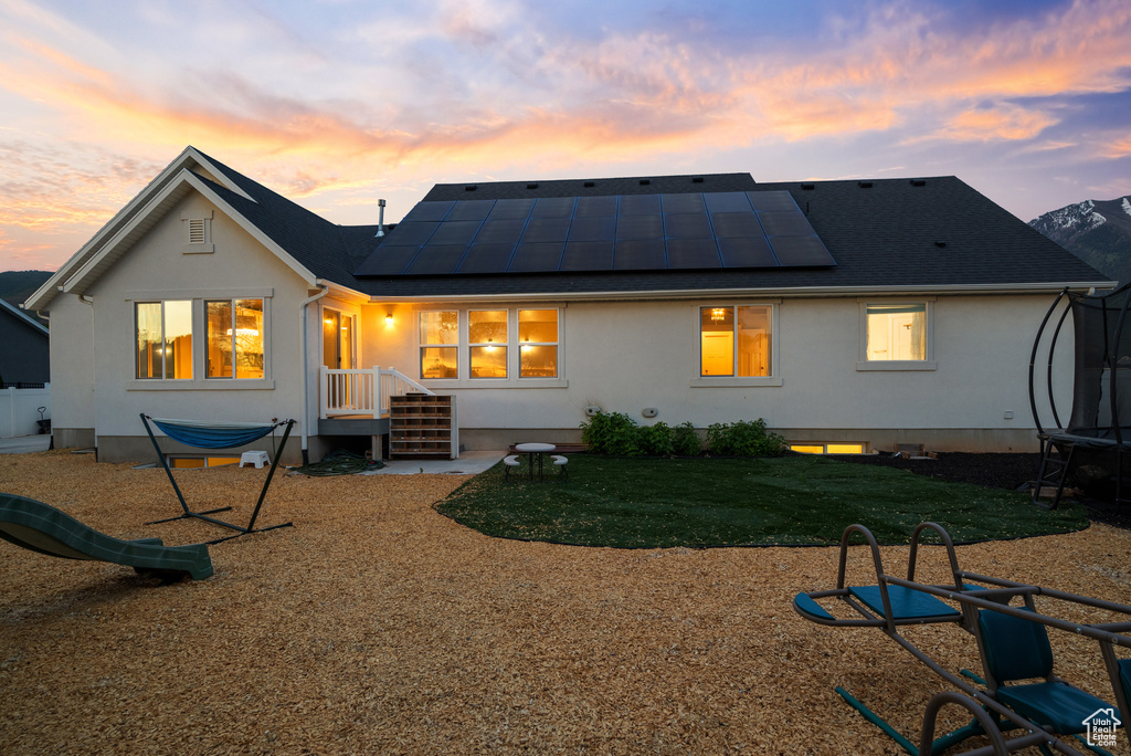 Back of property at dusk with a trampoline, roof mounted solar panels, a lawn, and stucco siding