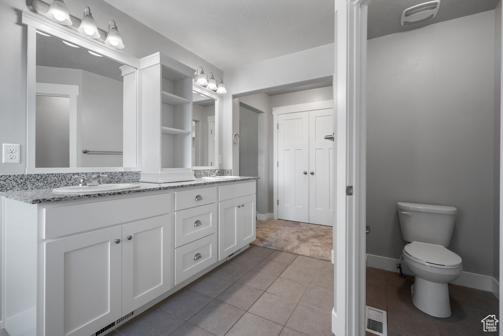 Full bath with double vanity, tile patterned floors, baseboards, and toilet