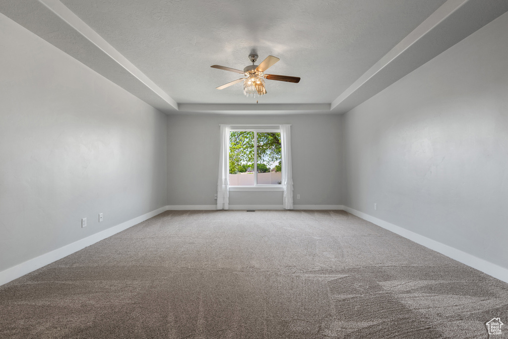 Carpeted spare room with a ceiling fan, baseboards, and a tray ceiling