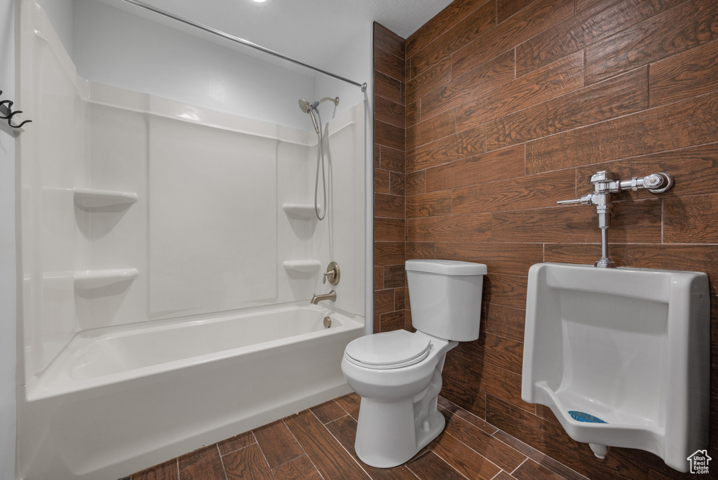 Full bathroom with bathtub / shower combination, toilet, wood walls, and wood finish floors
