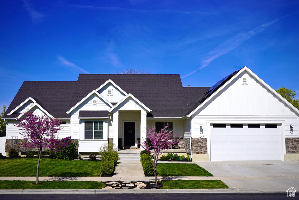 View of front of house featuring stone siding, board and batten siding, a garage, roof with shingles, and driveway