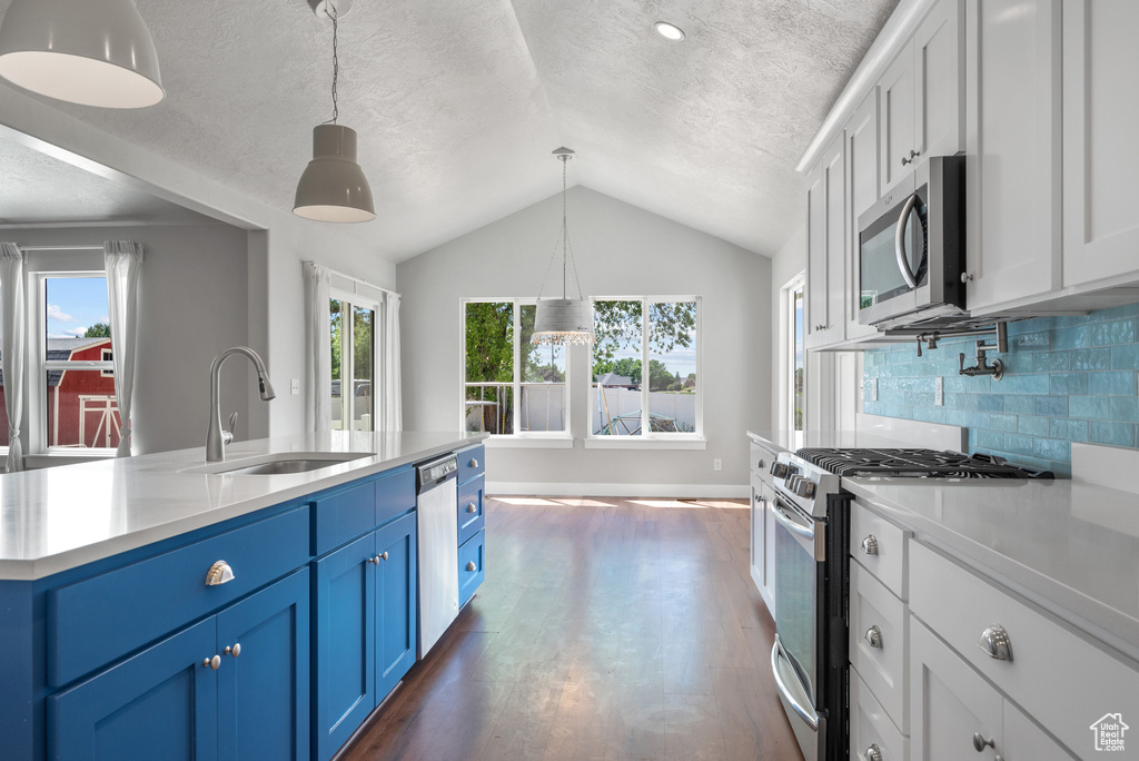Kitchen with stainless steel appliances, a sink, blue cabinets, lofted ceiling, and light countertops