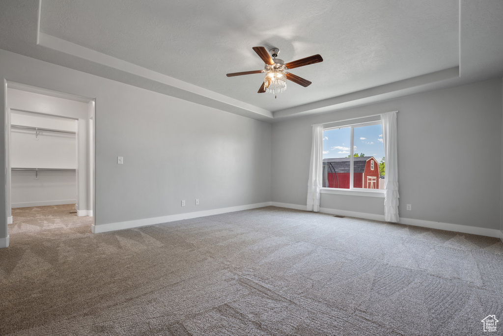 Carpeted spare room featuring a tray ceiling, ceiling fan, and baseboards