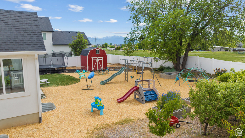 View of playground with a trampoline, a mountain view, and a fenced backyard