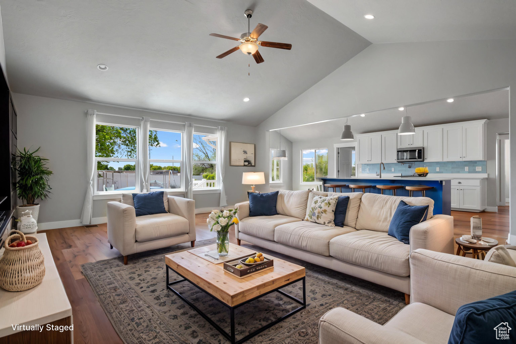 Living area with a ceiling fan, wood finished floors, high vaulted ceiling, recessed lighting, and baseboards