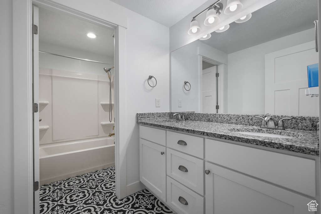 Full bathroom with double vanity, shower / bathtub combination, and baseboards