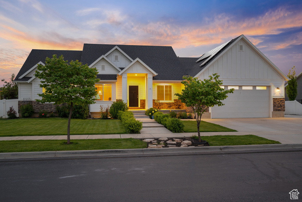 View of front of house with board and batten siding, stone siding, driveway, solar panels, and a garage