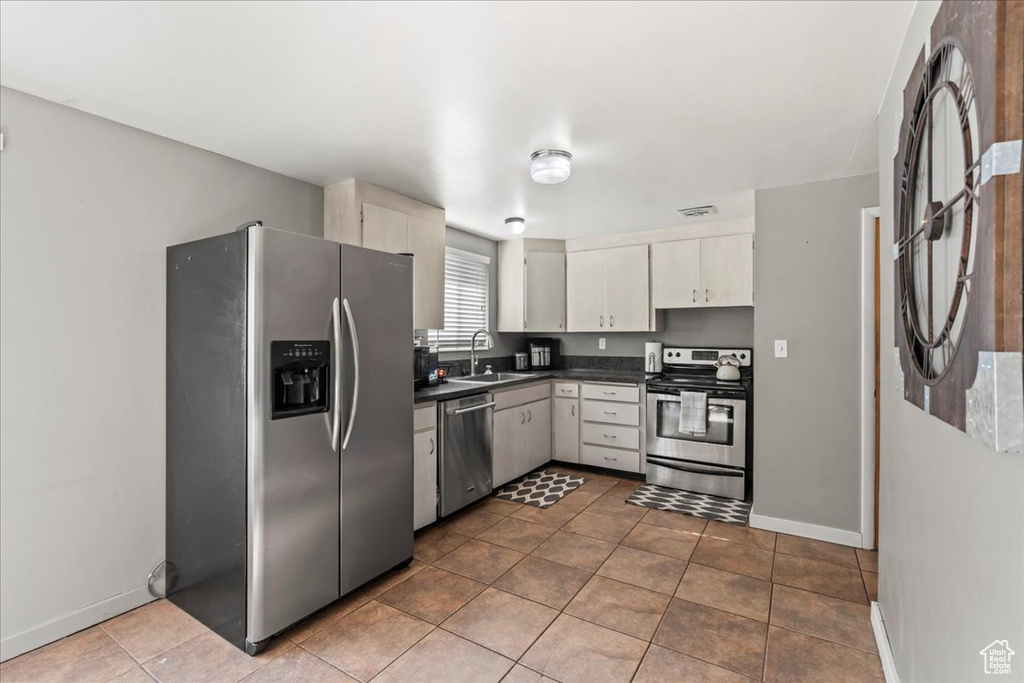 Kitchen featuring appliances with stainless steel finishes, a sink, dark countertops, baseboards, and tile patterned floors