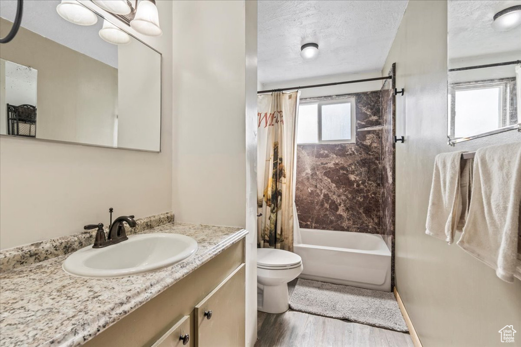 Full bath with toilet, shower / bathtub combination with curtain, vanity, wood finished floors, and a textured ceiling