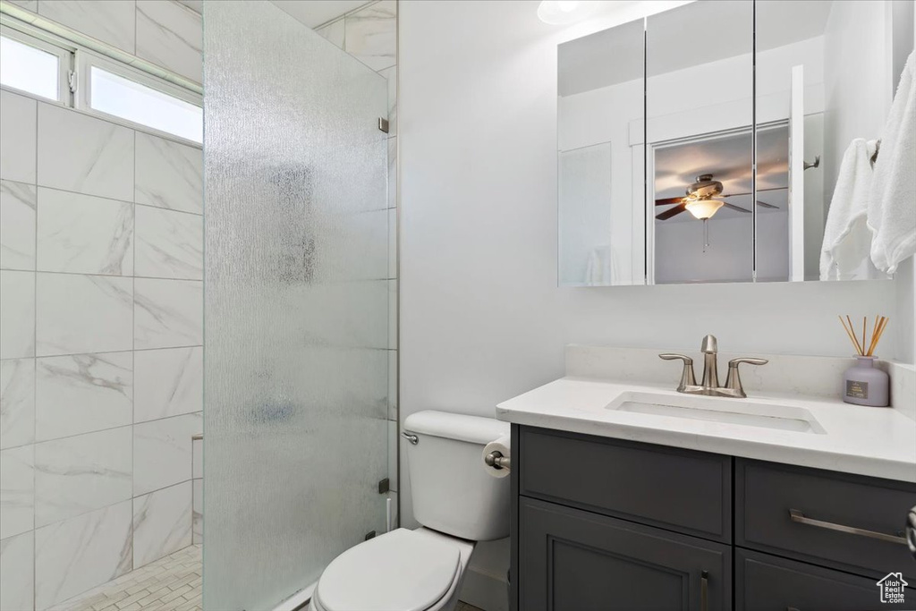 Full bath featuring toilet, vanity, a stall shower, ceiling fan, and baseboard heating