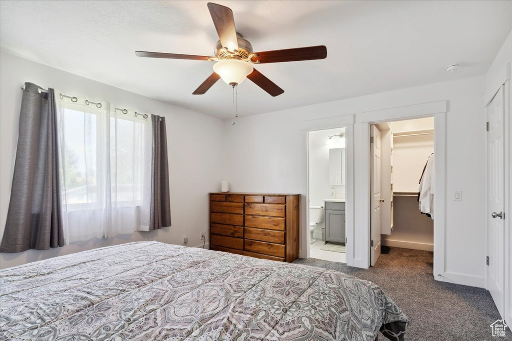 Carpeted bedroom with a spacious closet, a closet, a ceiling fan, ensuite bathroom, and baseboards