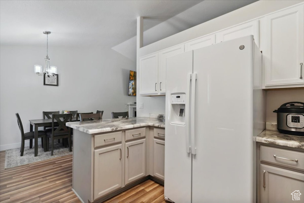 Kitchen with white refrigerator with ice dispenser, a peninsula, a chandelier, light wood finished floors, and pendant lighting