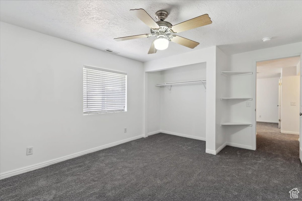 Unfurnished bedroom with dark colored carpet, a textured ceiling, a closet, baseboards, and ceiling fan