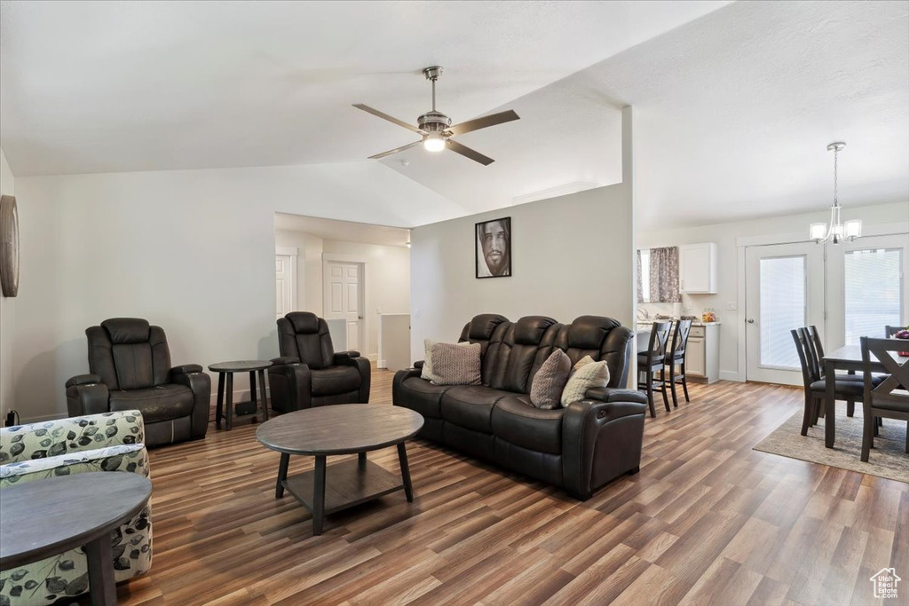 Living room featuring lofted ceiling, wood finished floors, ceiling fan, a chandelier, and baseboards