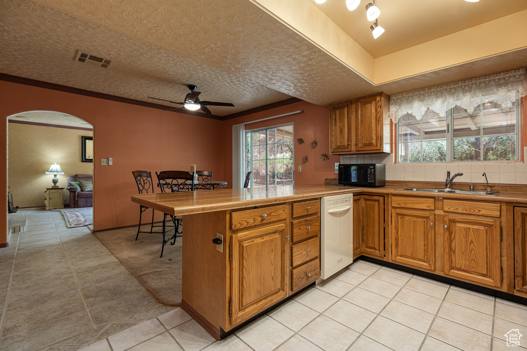 Kitchen with dishwasher, black microwave, a sink, brown cabinets, and a peninsula