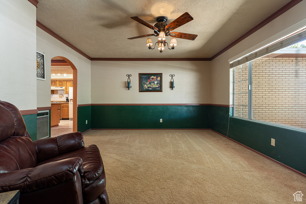 Living room with light colored carpet, a ceiling fan, ornamental molding, a wainscoted wall, and a textured ceiling
