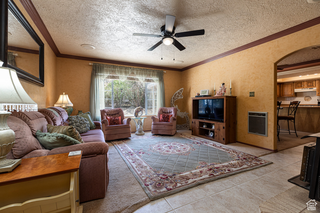 Living room with a ceiling fan, heating unit, tile patterned floors, a textured ceiling, and ornamental molding