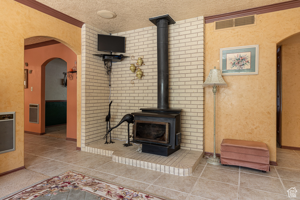 Tiled living room featuring a wood stove, heating unit, arched walkways, a textured ceiling, and a textured wall