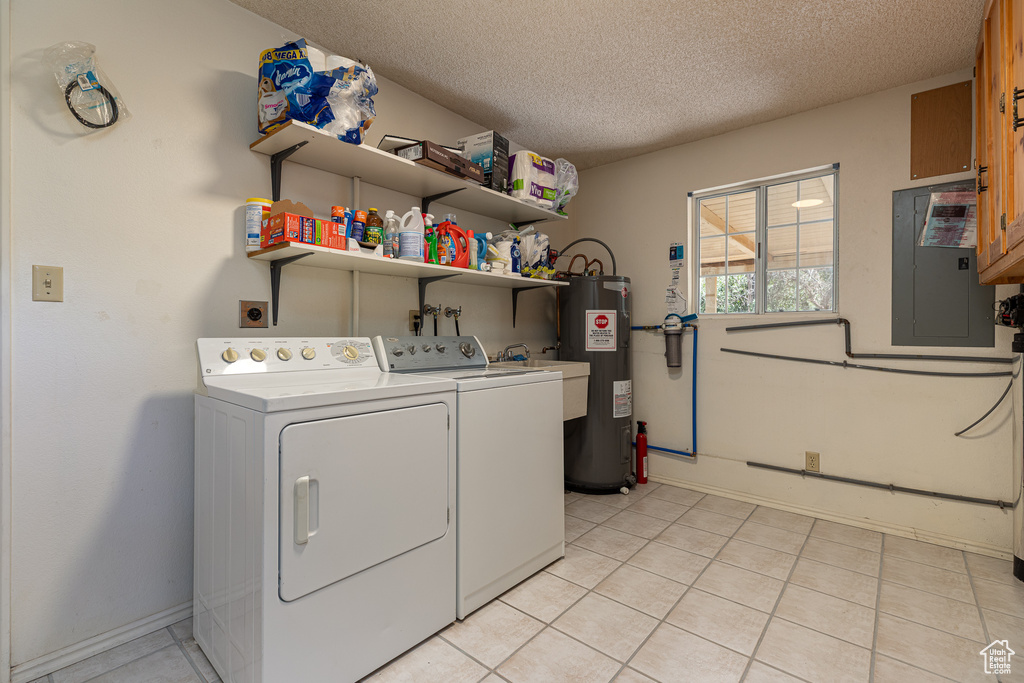 Laundry area with electric panel, washing machine and clothes dryer, electric water heater, a textured ceiling, and baseboards