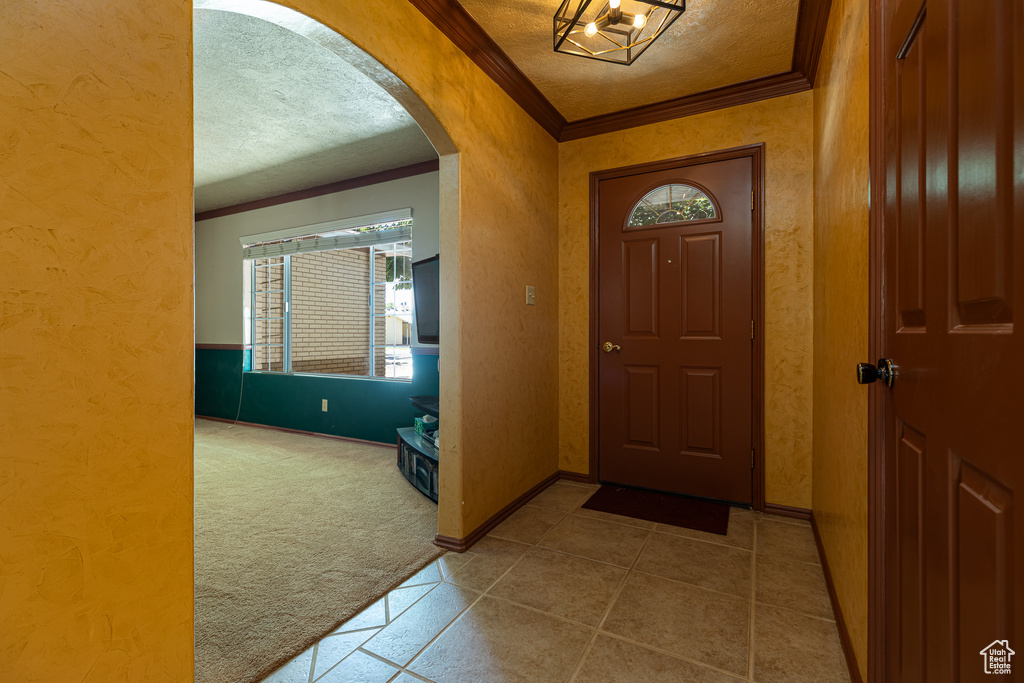 Carpeted entryway featuring crown molding, a textured ceiling, arched walkways, plenty of natural light, and a textured wall