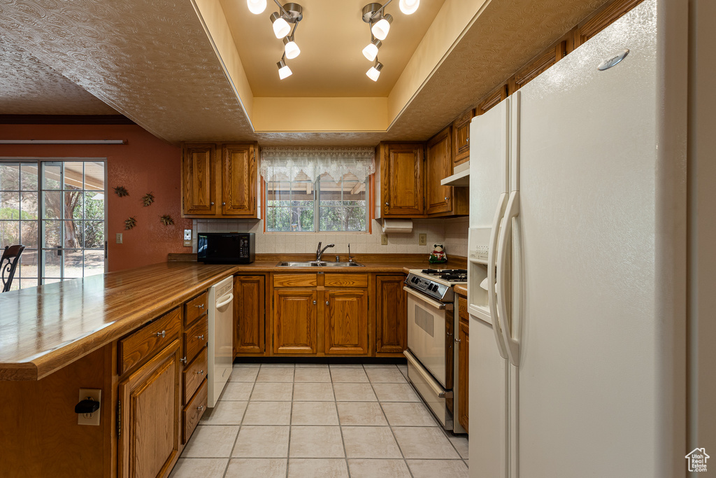 Kitchen featuring white fridge with ice dispenser, range with gas cooktop, brown cabinets, a peninsula, and dishwashing machine
