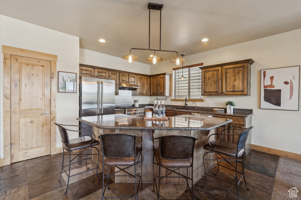 Kitchen with baseboards, under cabinet range hood, a sink, a center island, and a kitchen breakfast bar