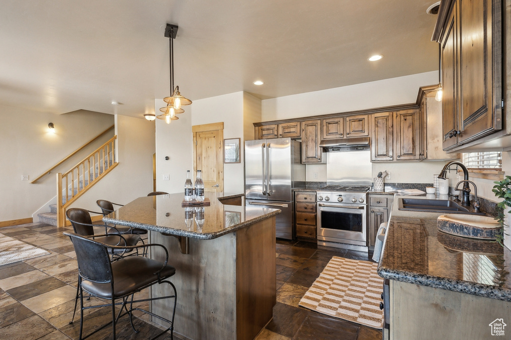 Kitchen with appliances with stainless steel finishes, a sink, a center island, a breakfast bar, and dark stone counters