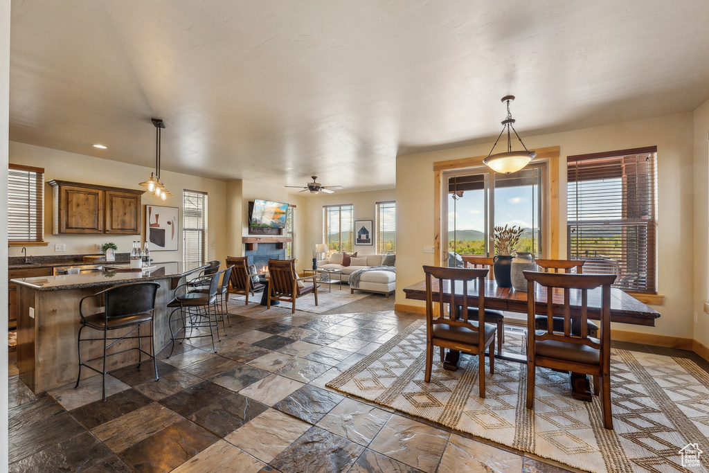 Dining room with healthy amount of natural light, baseboards, recessed lighting, ceiling fan, and a warm lit fireplace