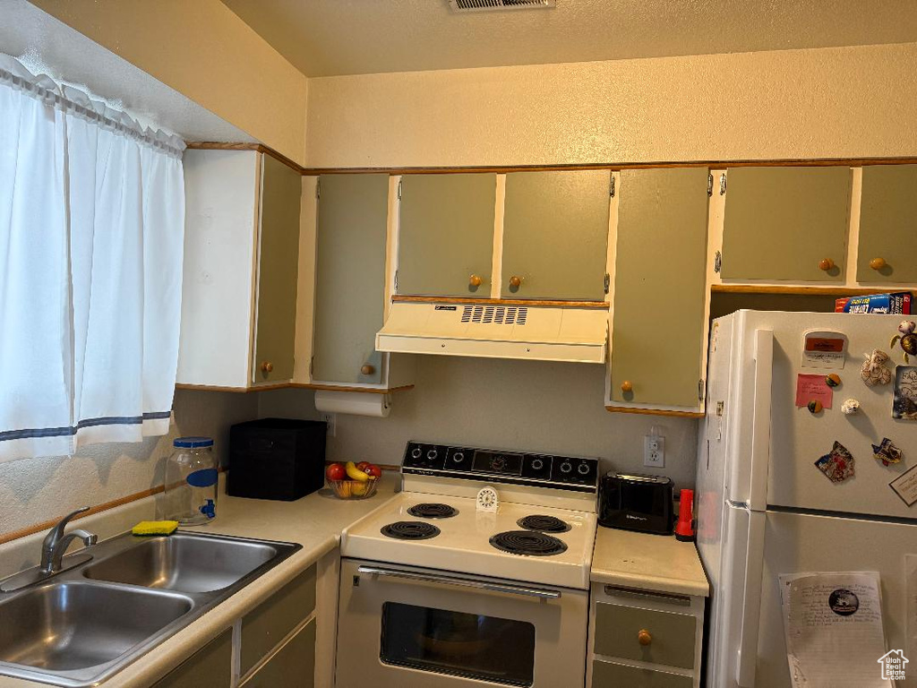 Kitchen with white appliances, under cabinet range hood, a sink, and light countertops