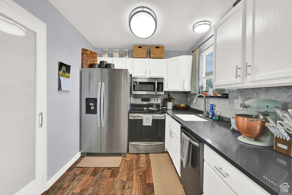 Kitchen with appliances with stainless steel finishes, a sink, dark countertops, dark wood finished floors, and backsplash