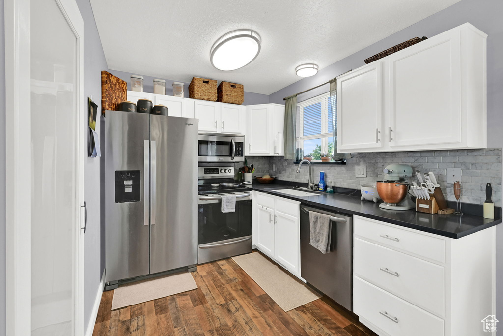 Kitchen with appliances with stainless steel finishes, dark countertops, a sink, and decorative backsplash