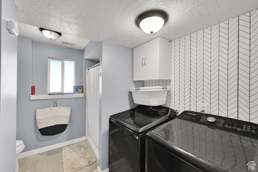 Laundry area with washer and dryer, a textured ceiling, and baseboards