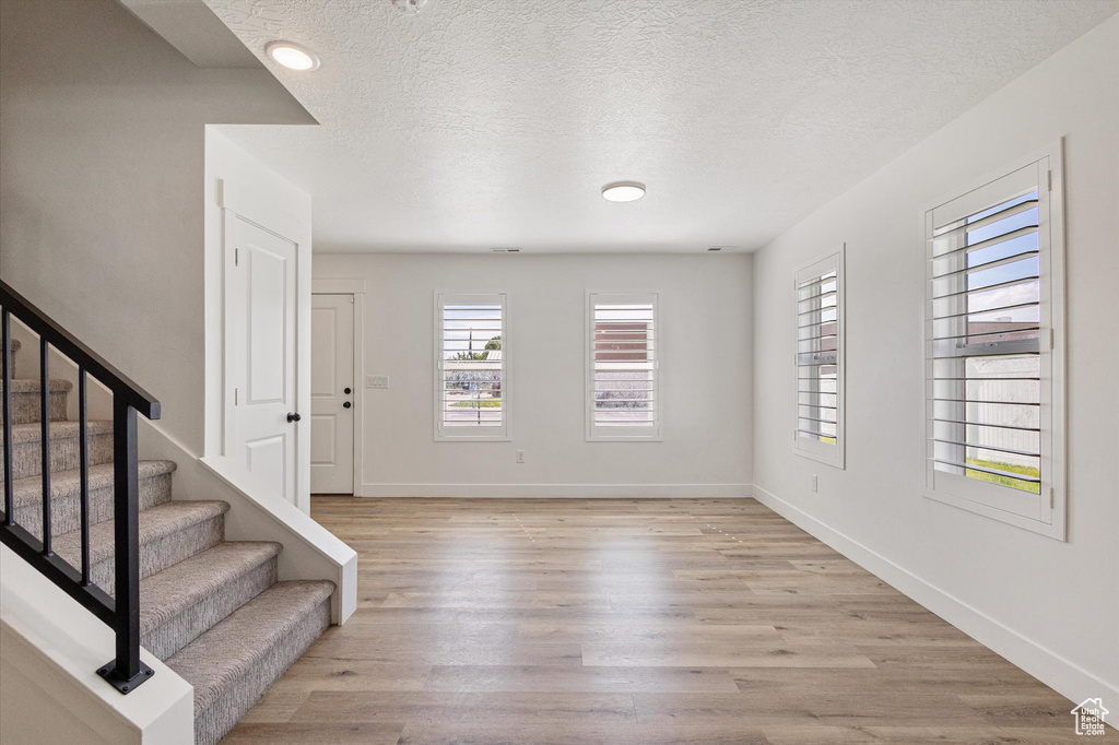 Entrance foyer featuring a textured ceiling, baseboards, light wood-style flooring, and stairs