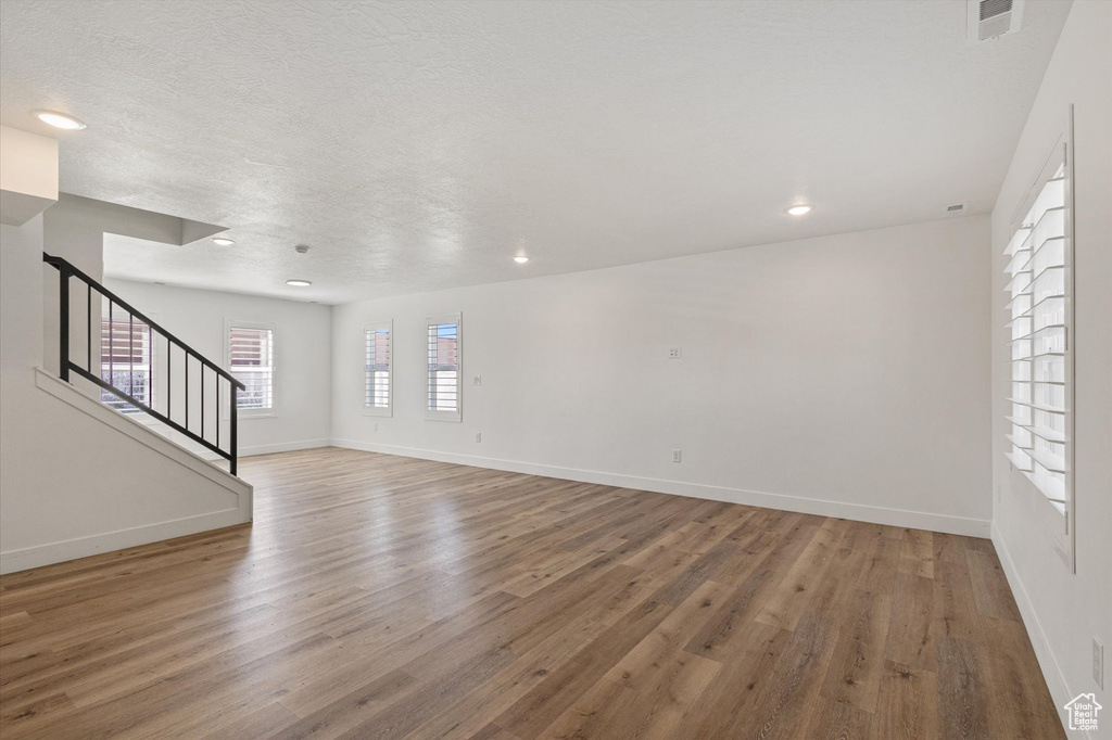Unfurnished living room featuring wood finished floors, stairs, baseboards, and recessed lighting