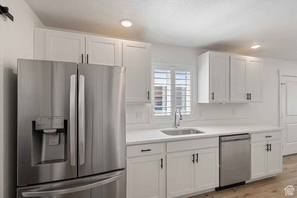 Kitchen with stainless steel appliances, a sink, white cabinetry, light wood-style floors, and recessed lighting