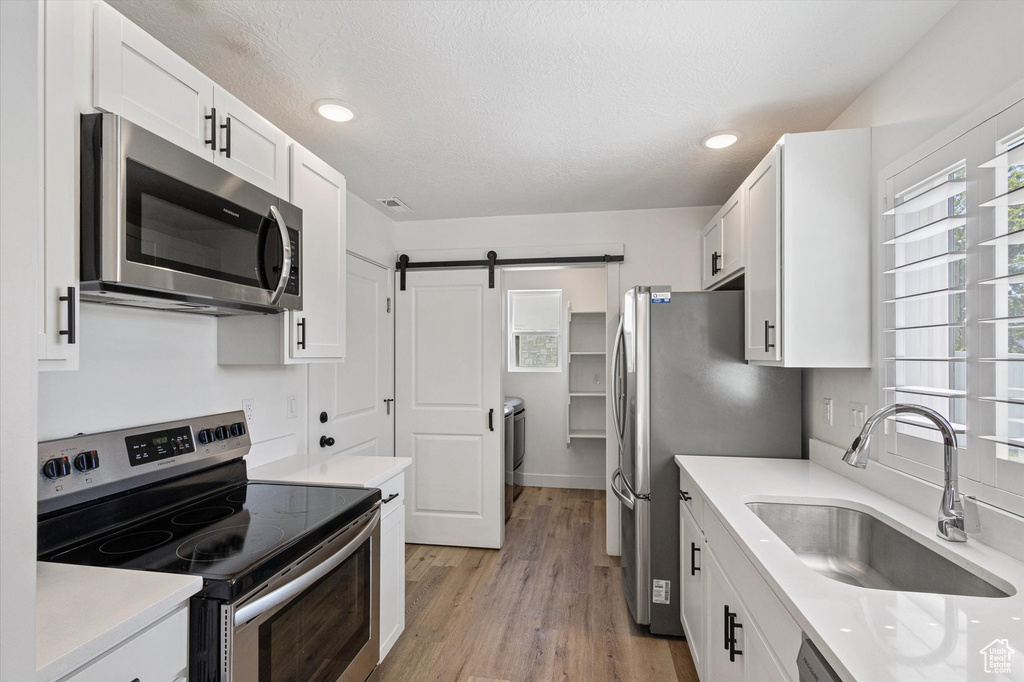 Kitchen with stainless steel appliances, a sink, white cabinetry, and recessed lighting