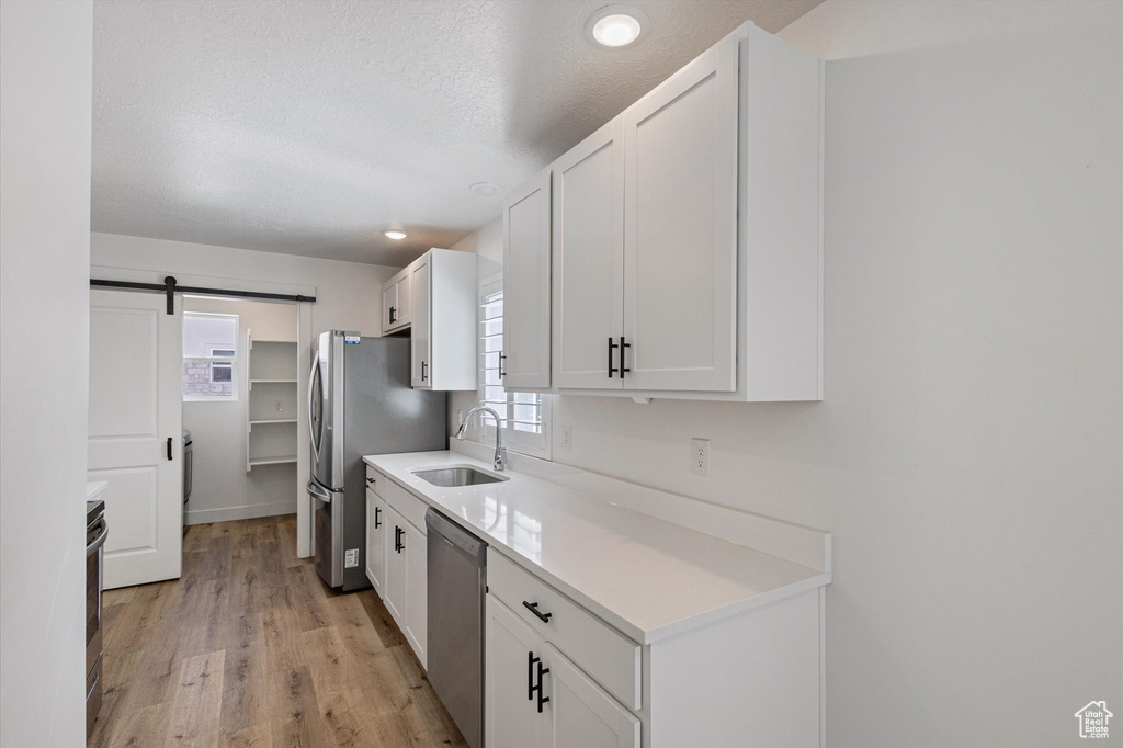 Kitchen featuring a sink, stainless steel appliances, light wood-style flooring, white cabinets, and light countertops