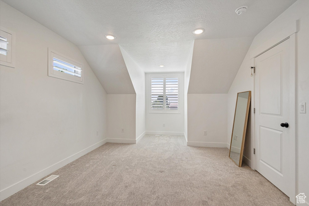 Additional living space with lofted ceiling, light colored carpet, baseboards, a textured ceiling, and recessed lighting