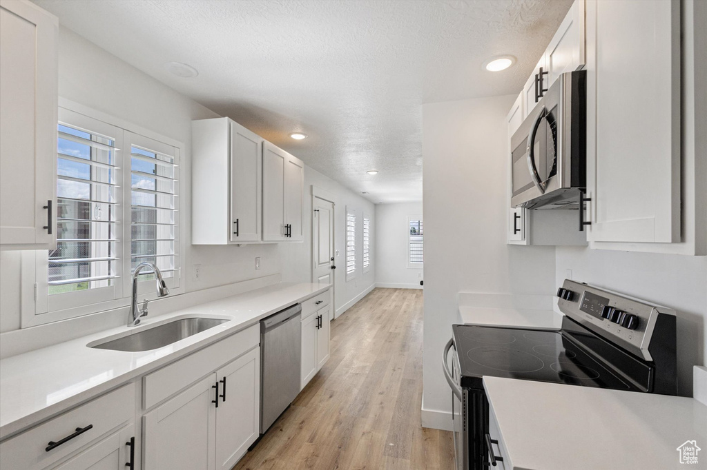 Kitchen with stainless steel appliances, a sink, light wood-style floors, white cabinets, and recessed lighting