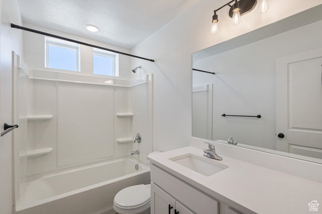 Full bathroom featuring toilet, vanity,  shower combination, and a textured ceiling