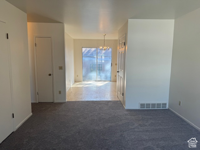 Carpeted empty room featuring a chandelier and baseboards