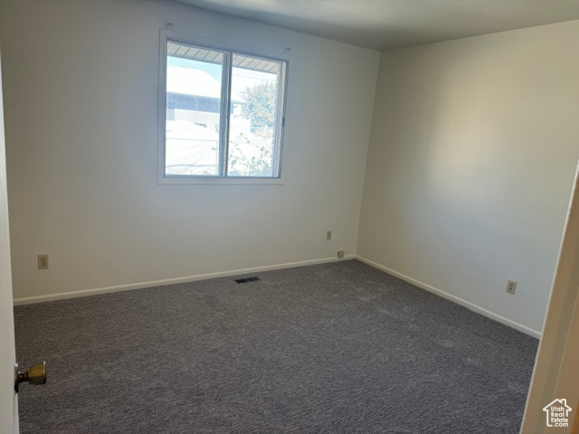 Unfurnished room featuring dark colored carpet and baseboards