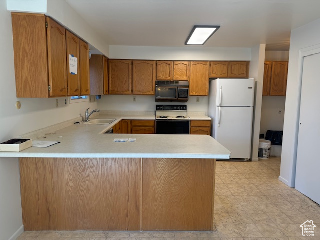 Kitchen with freestanding refrigerator, range with electric cooktop, a sink, a peninsula, and light countertops