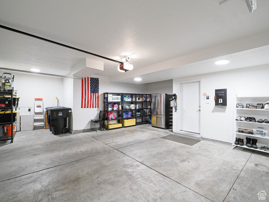 Garage with freestanding refrigerator, a garage door opener, and recessed lighting