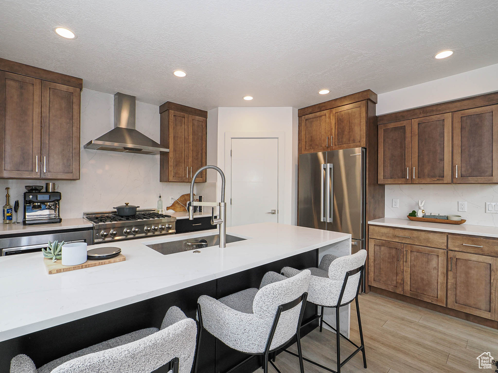 Kitchen featuring wall chimney exhaust hood, high end refrigerator, a sink, stove, and a kitchen bar