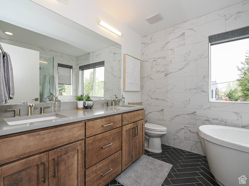 Full bathroom with tile walls, double vanity, a soaking tub, and toilet