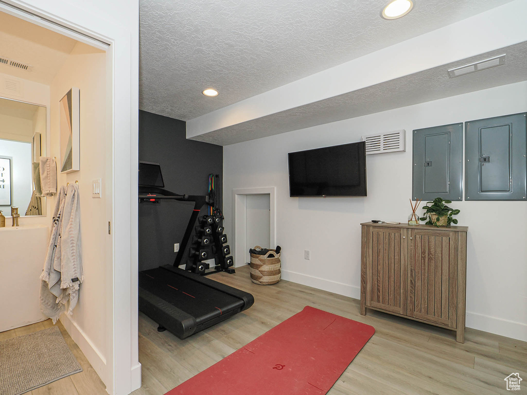 Workout area featuring baseboards, wood finished floors, recessed lighting, a textured ceiling, and electric panel
